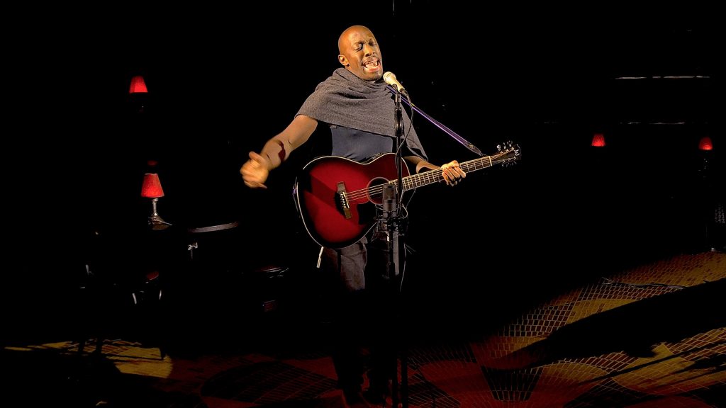 Giles Terera in BlackMatter standin gon the stag singing with a guitar in his left hand